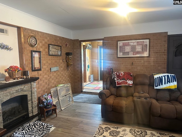 living room featuring hardwood / wood-style flooring, ornamental molding, brick wall, and a fireplace
