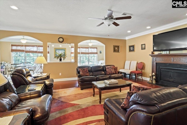 living room with ornamental molding, ceiling fan, a textured ceiling, and light wood-type flooring