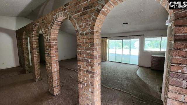 interior space with lofted ceiling, brick wall, carpet floors, and a textured ceiling