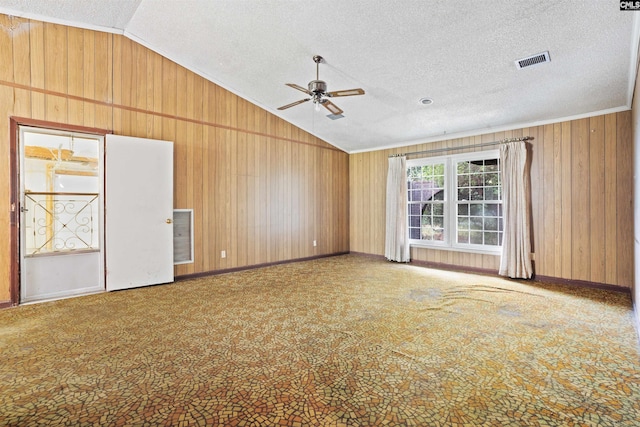 carpeted empty room featuring wood walls, ornamental molding, ceiling fan, a textured ceiling, and lofted ceiling