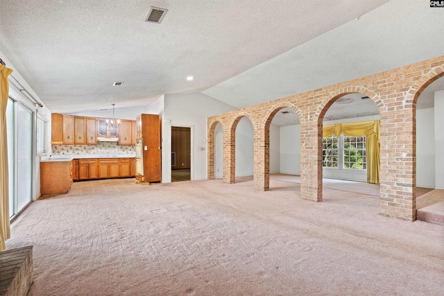 unfurnished living room featuring brick wall, a textured ceiling, light carpet, and vaulted ceiling