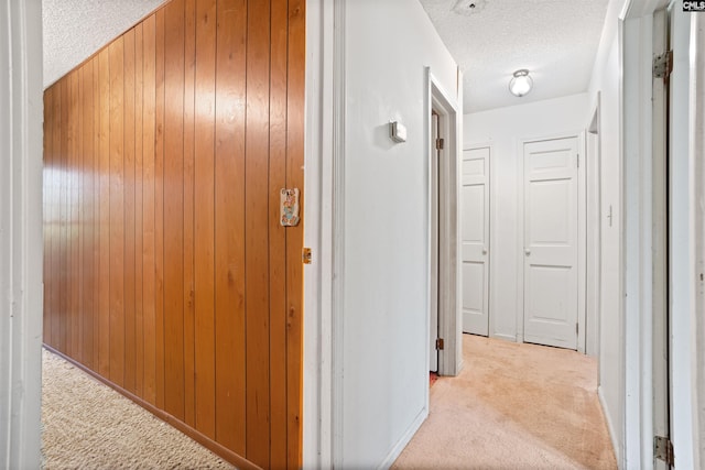 hall with wooden walls, light colored carpet, and a textured ceiling