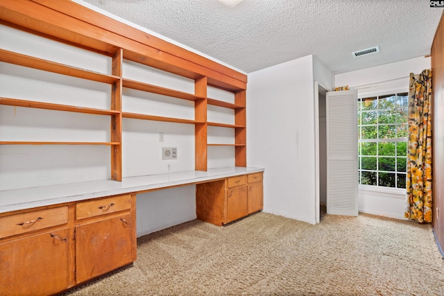 unfurnished office with light colored carpet, a textured ceiling, and built in desk