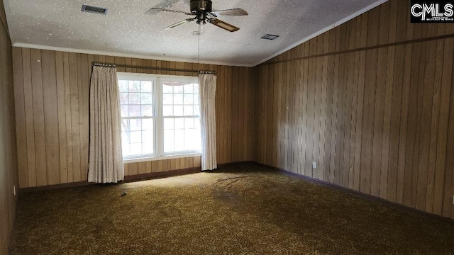 carpeted spare room featuring plenty of natural light, wooden walls, and a textured ceiling