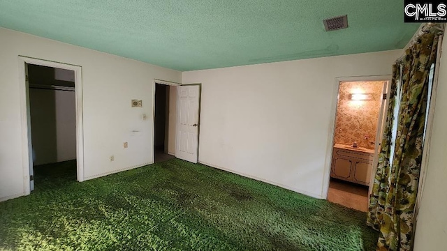 unfurnished bedroom with ensuite bath, dark carpet, a textured ceiling, and a closet