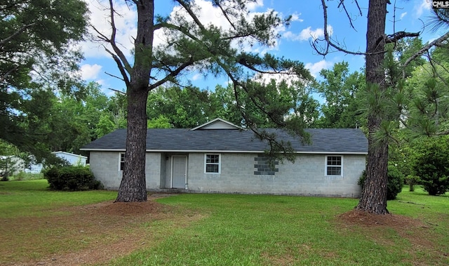 ranch-style home with roof with shingles, concrete block siding, and a front yard