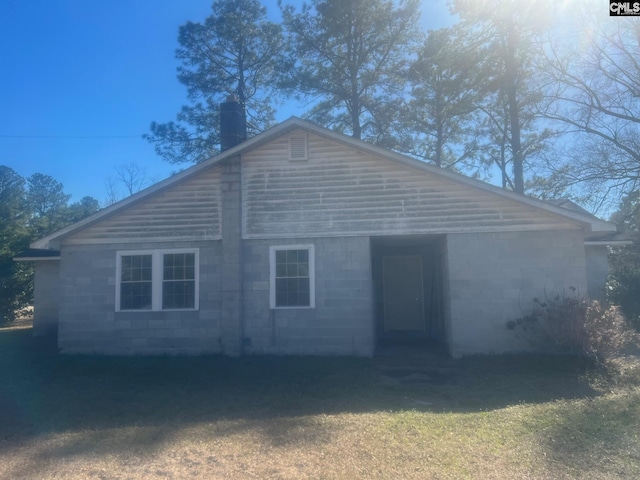 view of front facade featuring concrete block siding and a chimney