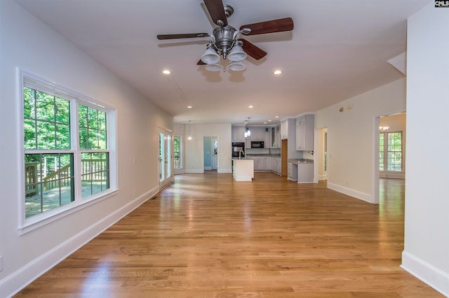 unfurnished living room with ceiling fan with notable chandelier, sink, and light hardwood / wood-style flooring