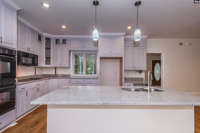 kitchen featuring sink, an island with sink, decorative light fixtures, black appliances, and light wood-type flooring