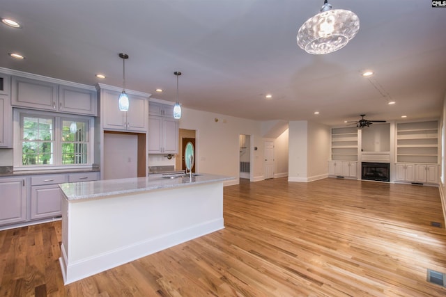 kitchen with pendant lighting, light hardwood / wood-style floors, sink, and an island with sink