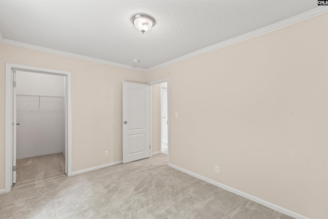 unfurnished bedroom featuring a spacious closet, light colored carpet, ornamental molding, a closet, and a textured ceiling