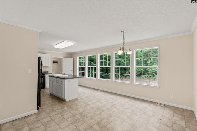 kitchen with a kitchen island with sink, a sink, white cabinets, hanging light fixtures, and dark countertops