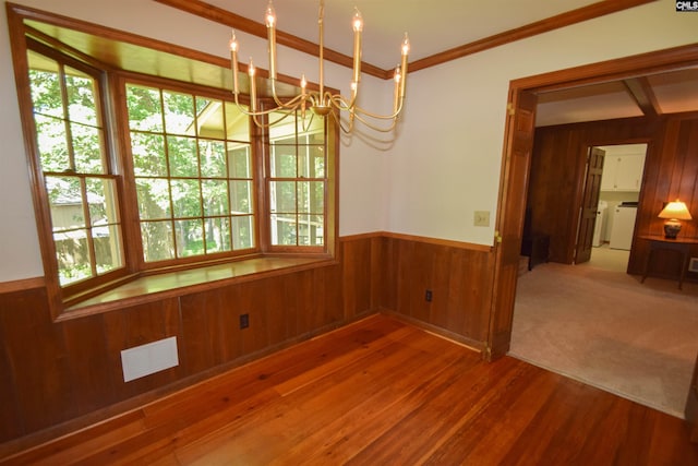 unfurnished dining area with hardwood / wood-style flooring, ornamental molding, a chandelier, and wood walls