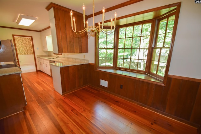 kitchen with an inviting chandelier, crown molding, stainless steel refrigerator, wooden walls, and light hardwood / wood-style floors