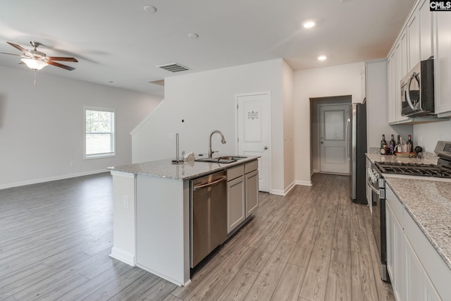 kitchen featuring sink, stainless steel appliances, light stone counters, an island with sink, and light hardwood / wood-style floors