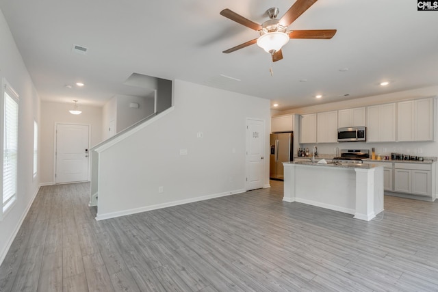 kitchen with light wood-type flooring, stainless steel appliances, ceiling fan, a center island with sink, and white cabinetry