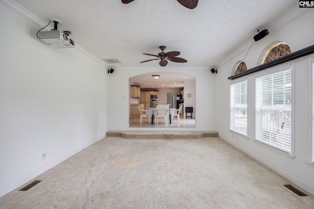 unfurnished living room featuring a textured ceiling, ornamental molding, carpet floors, and ceiling fan