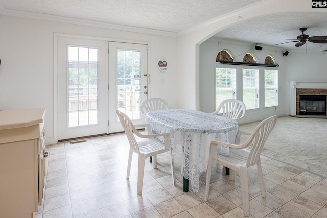 dining space with a textured ceiling, a fireplace, ornamental molding, ceiling fan, and light tile floors