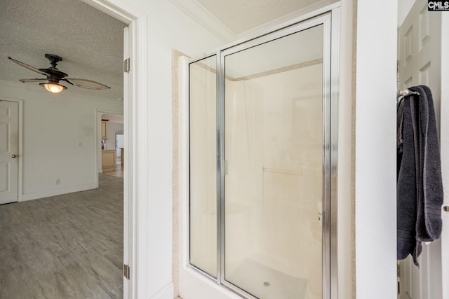 bathroom with ceiling fan, crown molding, an enclosed shower, wood-type flooring, and a textured ceiling