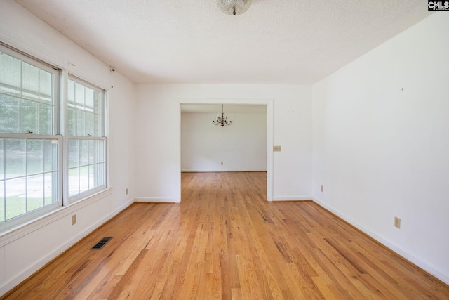 empty room featuring a chandelier and light wood-type flooring