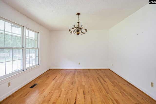 spare room with a healthy amount of sunlight, light hardwood / wood-style floors, a textured ceiling, and a chandelier