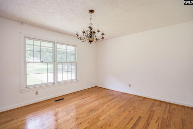 empty room with a healthy amount of sunlight, a chandelier, and light hardwood / wood-style flooring