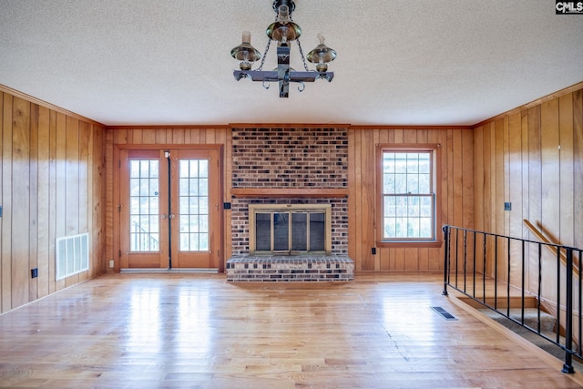 unfurnished living room featuring brick wall, light hardwood / wood-style floors, a notable chandelier, wood walls, and a textured ceiling