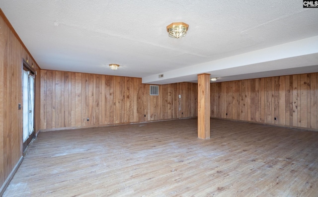 basement featuring wooden walls, light hardwood / wood-style floors, and a textured ceiling