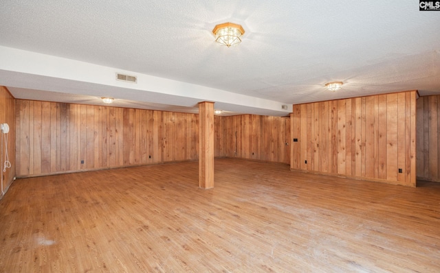 basement with wooden walls, light hardwood / wood-style floors, and a textured ceiling