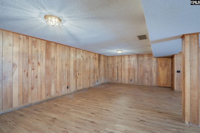 basement featuring wooden walls, light hardwood / wood-style floors, and a textured ceiling