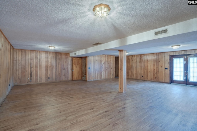 basement featuring french doors, wood-type flooring, wood walls, and a textured ceiling