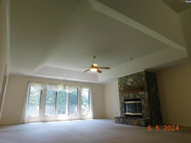 unfurnished living room featuring a tray ceiling, ceiling fan, a fireplace, and carpet