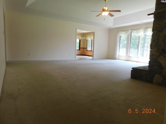 unfurnished living room featuring carpet, ceiling fan with notable chandelier, and a tray ceiling