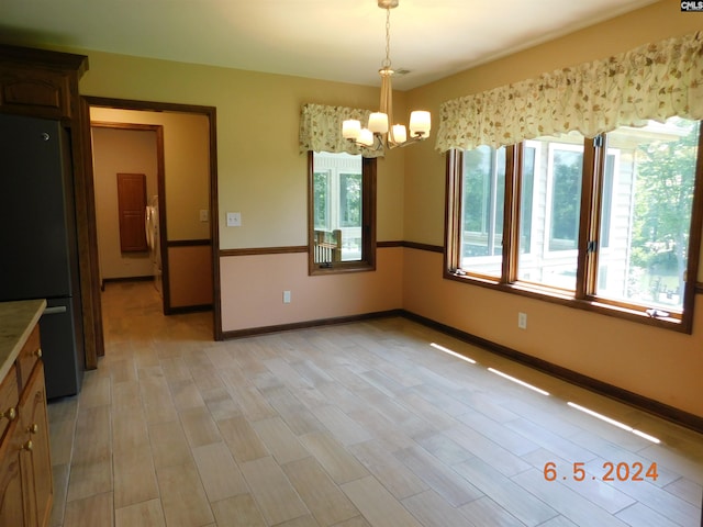 unfurnished dining area with a chandelier and light wood-type flooring