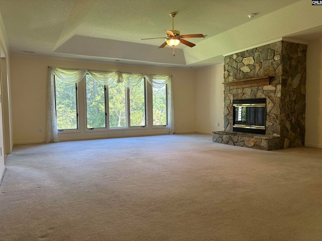 unfurnished living room featuring a tray ceiling, a stone fireplace, light carpet, and ceiling fan