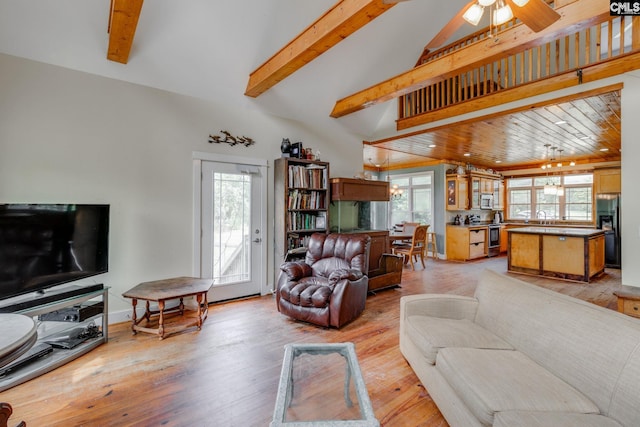 living area featuring light wood-type flooring, a ceiling fan, and beam ceiling