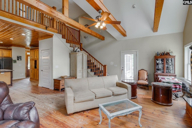 living area featuring high vaulted ceiling, a ceiling fan, light wood-style floors, stairway, and beam ceiling