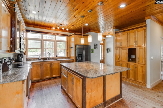 kitchen featuring stone countertops, a kitchen island, decorative light fixtures, refrigerator with ice dispenser, and a sink