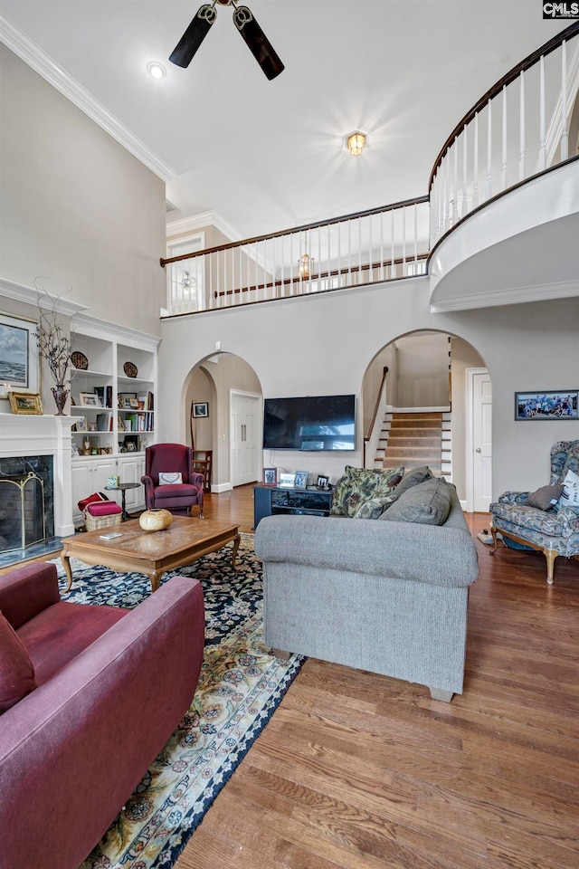 living room featuring a premium fireplace, wood-type flooring, ceiling fan, and a high ceiling