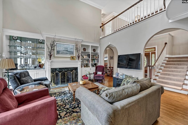 living room with a fireplace, wood-type flooring, built in features, a towering ceiling, and ornamental molding