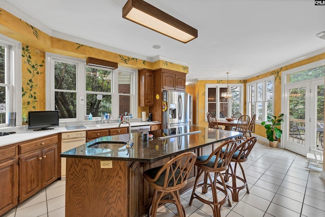 kitchen featuring a kitchen breakfast bar, stainless steel fridge, decorative light fixtures, light tile floors, and a kitchen island with sink