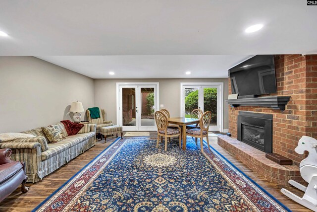 living room featuring french doors, a fireplace, hardwood / wood-style flooring, and brick wall