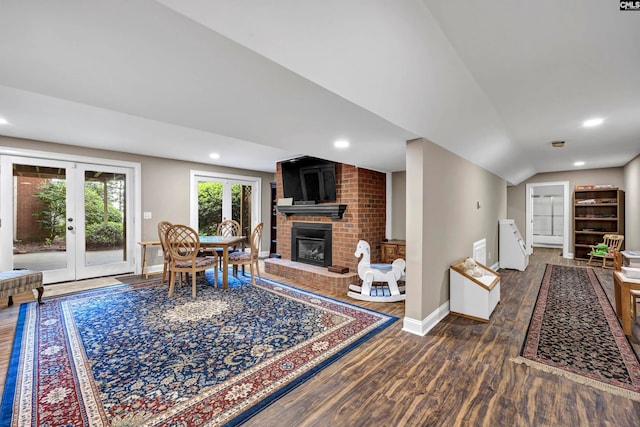 living room with french doors, brick wall, dark hardwood / wood-style floors, a brick fireplace, and vaulted ceiling