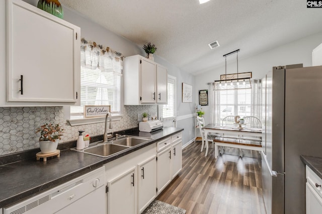 kitchen with stainless steel refrigerator, sink, white dishwasher, vaulted ceiling, and white cabinets