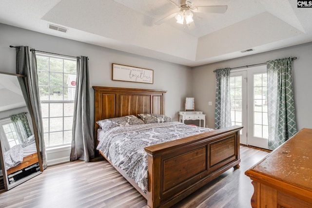 bedroom with ceiling fan, a raised ceiling, light hardwood / wood-style flooring, and multiple windows