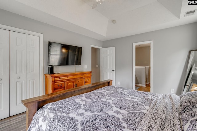 bedroom with a closet, light hardwood / wood-style flooring, and a tray ceiling