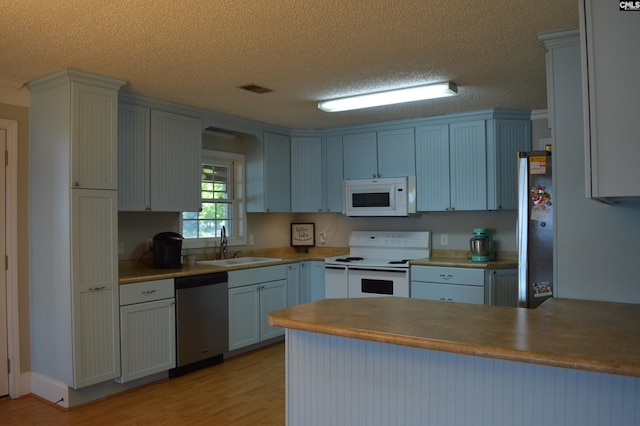 kitchen with sink, kitchen peninsula, a textured ceiling, appliances with stainless steel finishes, and light wood-type flooring