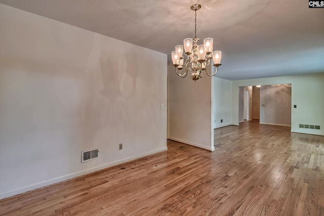 unfurnished dining area featuring a textured ceiling, a notable chandelier, and light wood-type flooring