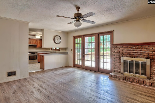 unfurnished living room featuring a brick fireplace, a textured ceiling, light hardwood / wood-style flooring, and ceiling fan