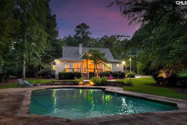 pool at dusk featuring a yard and a patio